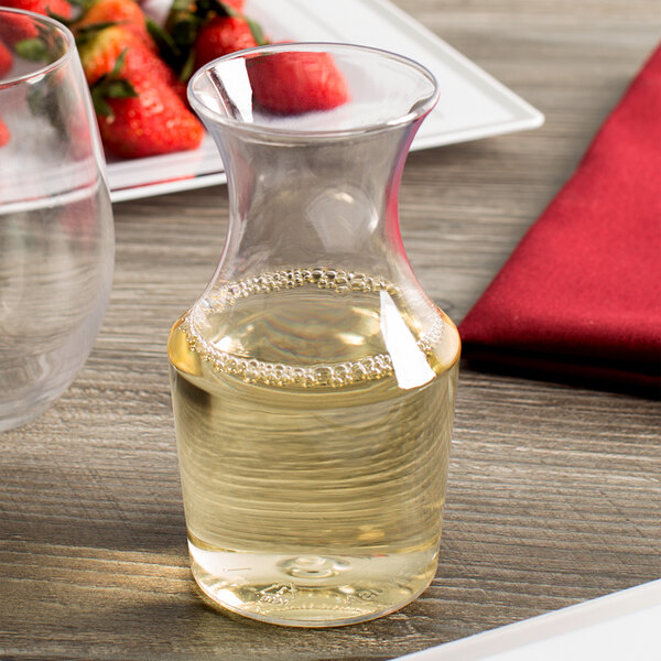 A WNA Comet clear plastic wine carafe on a table with a glass of wine.