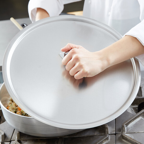 A person holding a Vollrath domed aluminum pot cover over a pan.