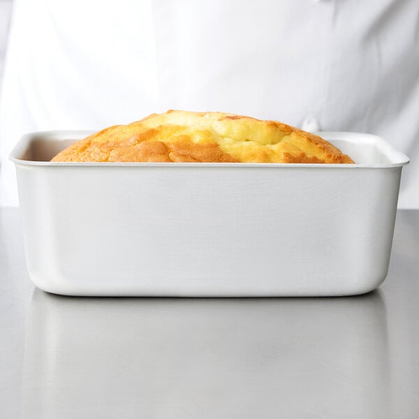 A Vollrath white aluminum bread loaf pan with a baked loaf of bread.
