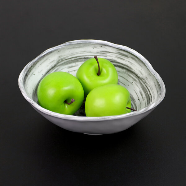 A black Elite Global Solutions oval melamine bowl filled with green apples.