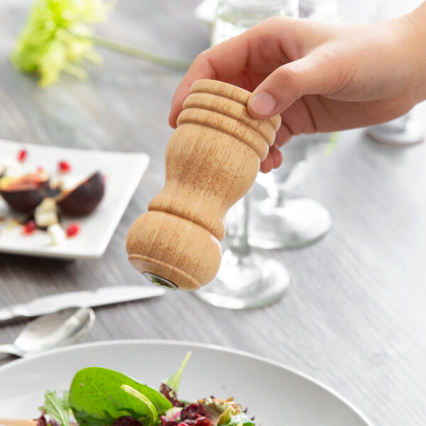 A hand holding a Acopa wooden salt shaker over a plate of food.