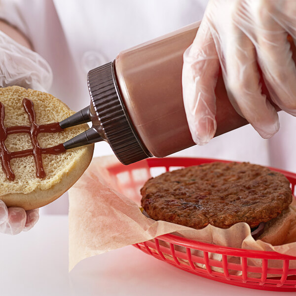 A gloved hand pouring brown sauce from a Vollrath Twin Tip squeeze bottle onto a hamburger.