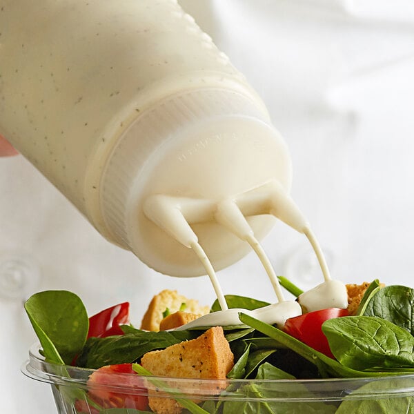 A close-up of a salad being poured from a Vollrath Clear Tri Tip Squeeze Bottle onto a salad.