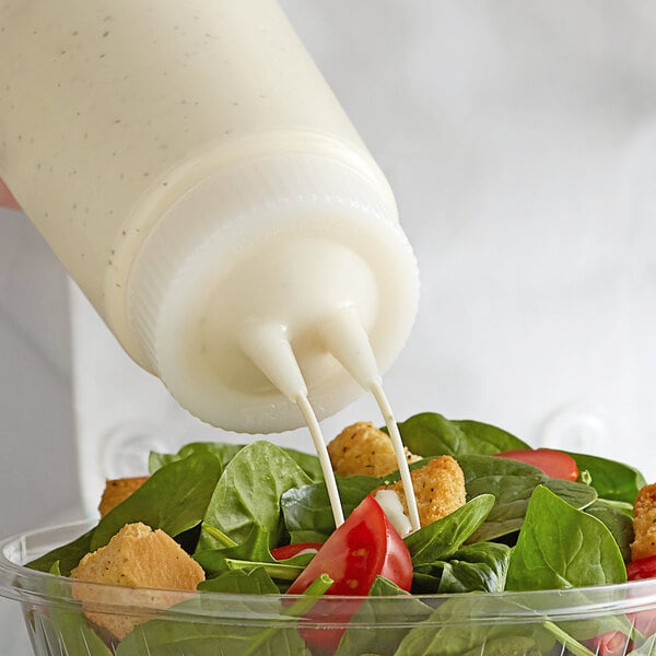 A person using a Vollrath Twin Tip Squeeze Bottle to pour dressing on a salad.