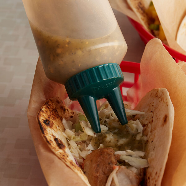 A clear plastic Vollrath Twin Tip squeeze bottle with Vista Green cap pouring sauce on a tortilla.