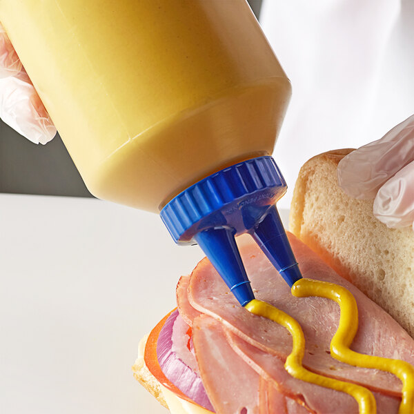 A person using a Vollrath Twin Tip Squeeze Bottle to put mustard on a sandwich.
