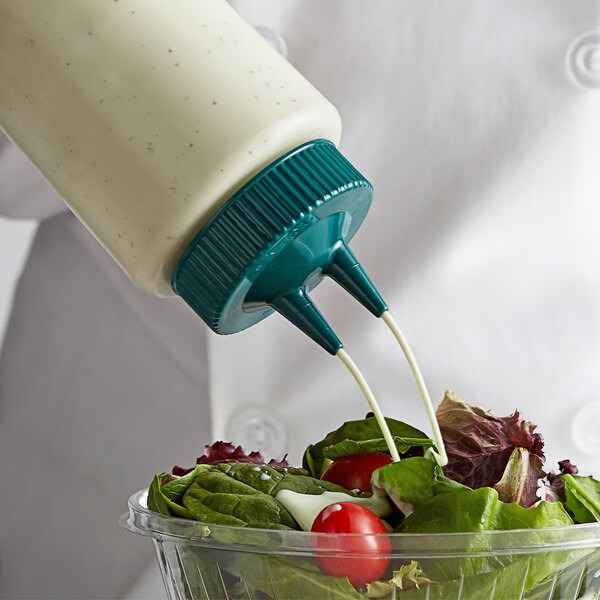 A person pouring dressing from a Vollrath Twin Tip Squeeze Bottle with a Vista Green cap onto a salad.