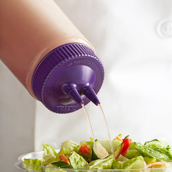 A person using a Vollrath Color-Mate Twin Tip Squeeze Bottle with purple cap to pour sauce over a salad.
