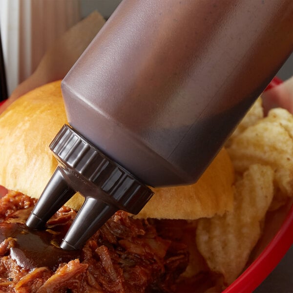 A close-up of a clear Vollrath Twin Tip squeeze bottle with brown liquid being poured into a bowl of pulled pork.