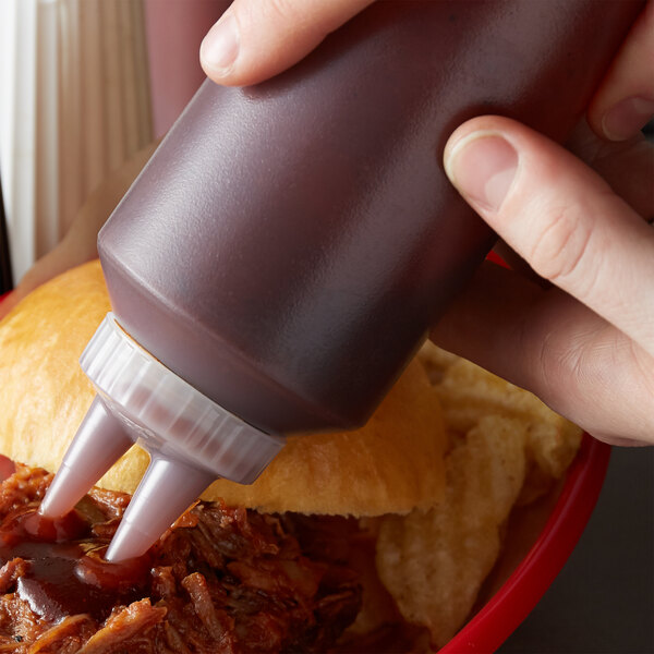 A hand using a Vollrath Twin Tip squeeze bottle to pour barbecue sauce onto a burger.