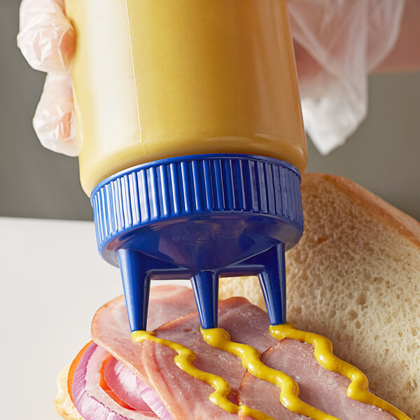 A hand using a Vollrath Clear Tri Tip Squeeze Bottle with a blue lid to put mustard on a sandwich.