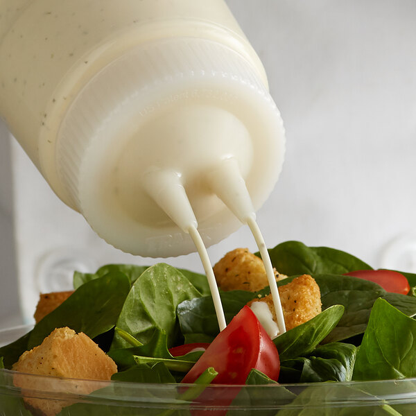 A salad with dressing being poured into a clear plastic container with a green Vollrath Twin Tip bottle cap.