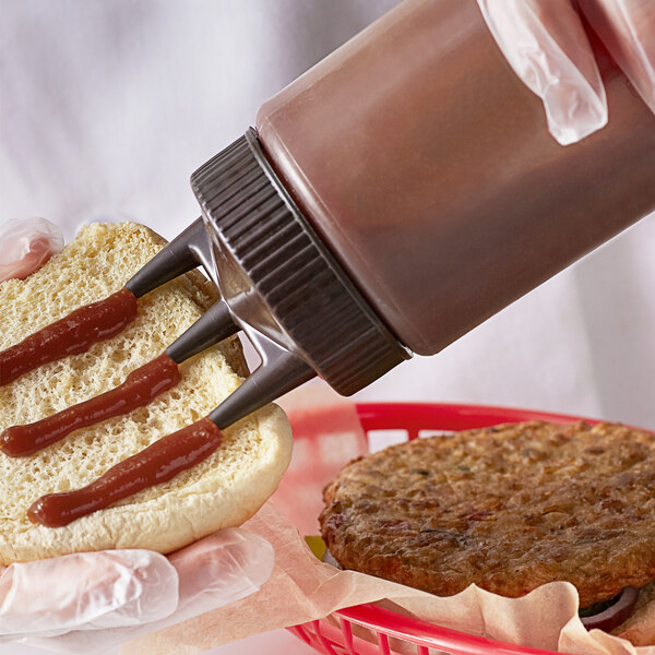 A person using a Vollrath Tri Tip squeeze bottle to put ketchup on a hamburger.
