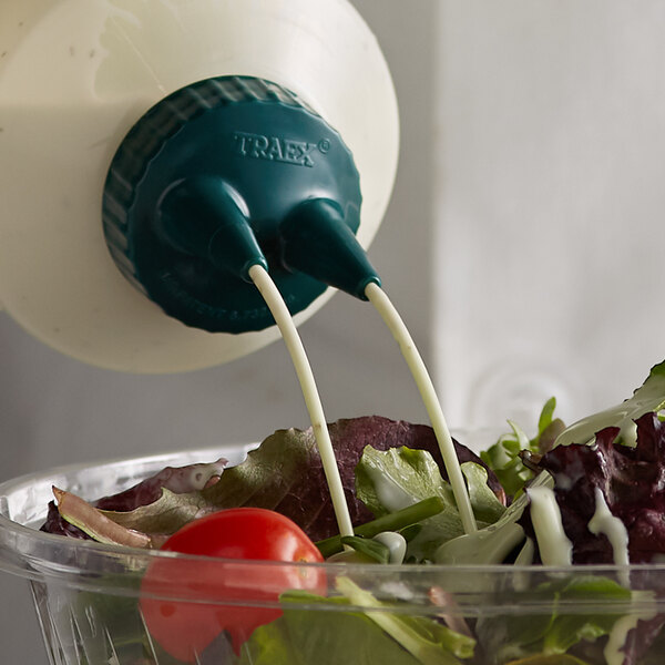 A tomato being placed in a container with a Vollrath Traex Vista Green Twin Tip Bottle Cap.