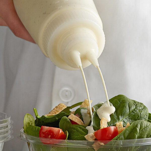 A person using a Vollrath wide mouth squeeze bottle to pour dressing on a salad.