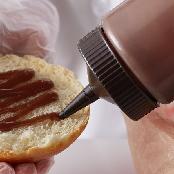 A person putting chocolate sauce on a bun using a Vollrath Traex wide mouth bottle cap.