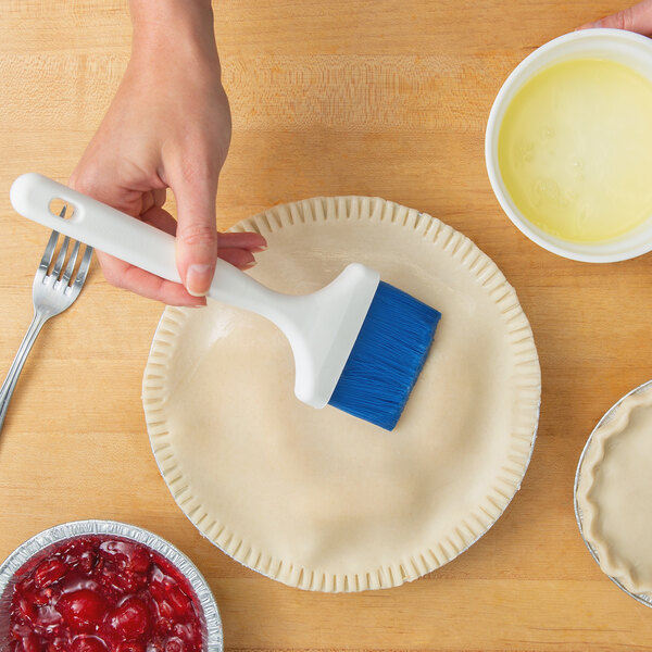 A hand using a Carlisle Sparta Spectrum blue pastry brush to baste a pie crust.