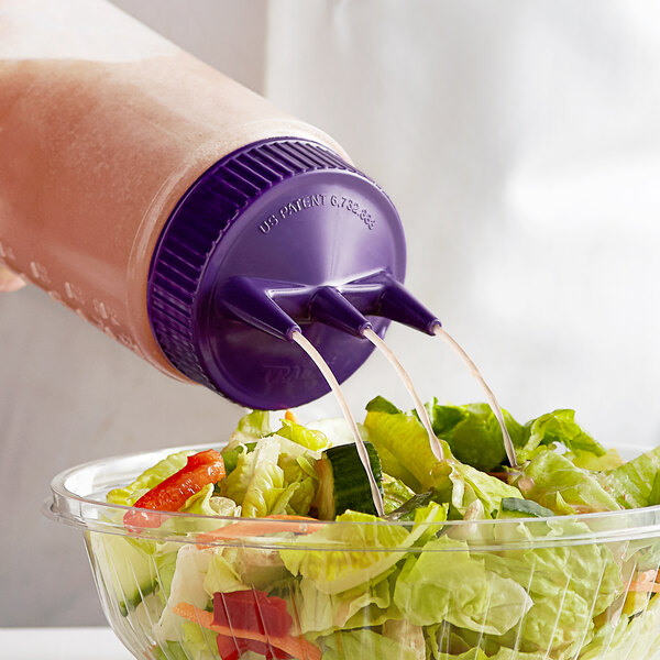 A person pouring purple liquid from a Vollrath Tri Tip squeeze bottle with a purple cap onto a salad.
