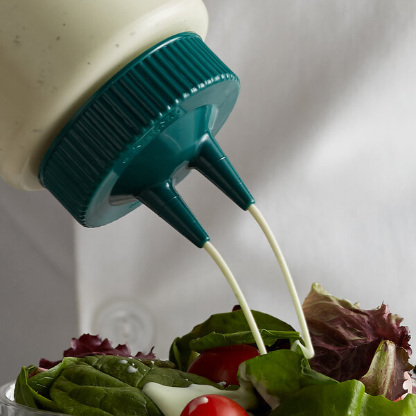 A close up of a Vollrath Traex Vista Green Twin Tip Wide Mouth Bottle Cap pouring mayonnaise onto a green salad.