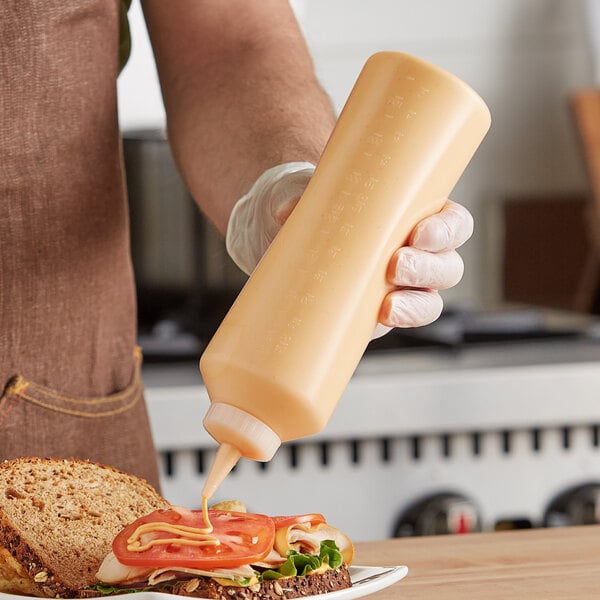 A person using a Vollrath clear squeeze bottle to pour mustard on a sandwich.