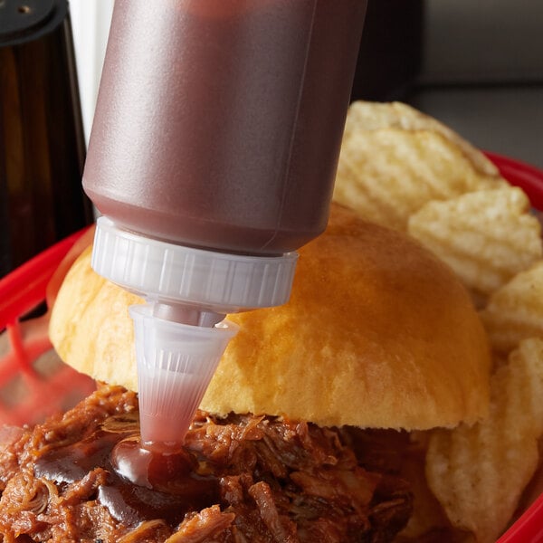 A person using a Vollrath clear squeeze bottle to pour barbecue sauce on a sandwich.