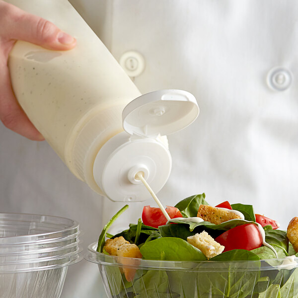 A hand squeezing Vollrath clear wide mouth squeeze bottle to pour dressing on a salad.
