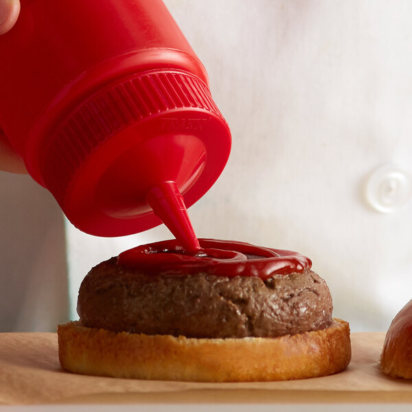 A person pouring Vollrath red wide mouth bottle cap onto a burger.