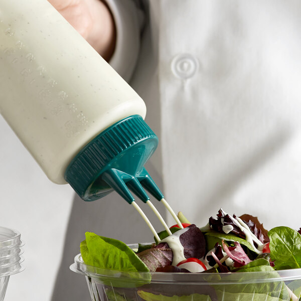 A person using a Vollrath Tri Tip squeeze bottle to pour dressing onto a salad.