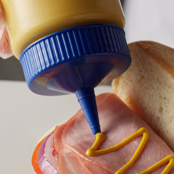 A person using a Vollrath blue wide mouth bottle cap to pour mustard on a sandwich.