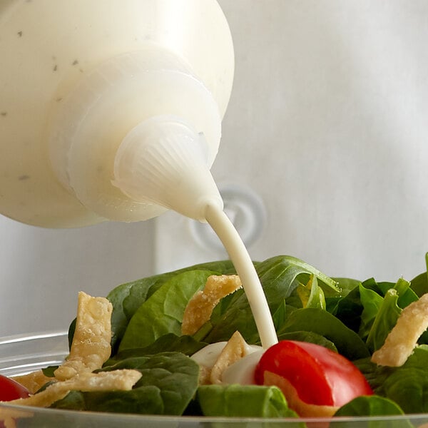 A Vollrath Traex clear squeeze bottle pouring sauce onto a salad.
