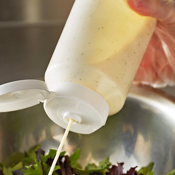 A close-up of a Vollrath Traex squeeze bottle pouring dressing into a container.