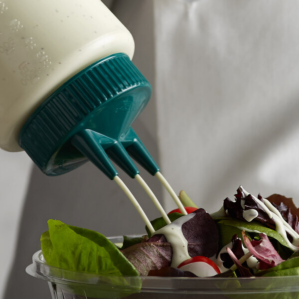 A person using a Vollrath Tri Tip bottle cap to pour dressing onto a salad.