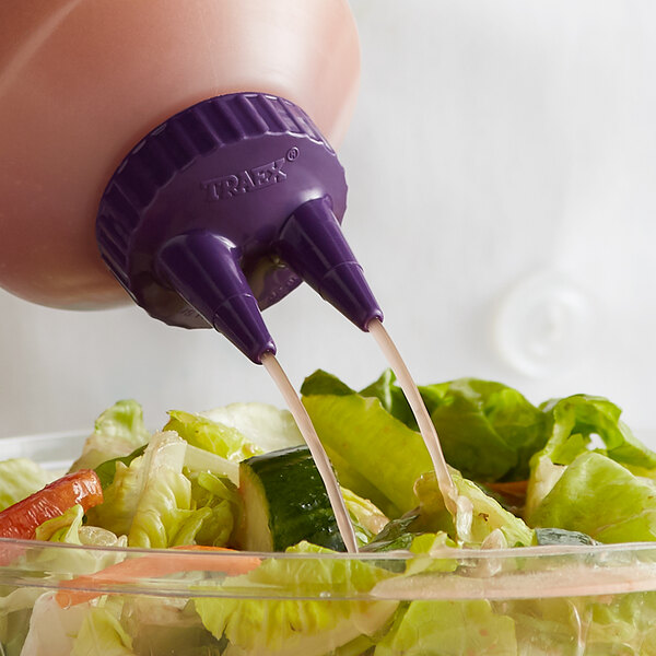 A purple Vollrath Twin Tip bottle cap pouring liquid into a bowl of salad.