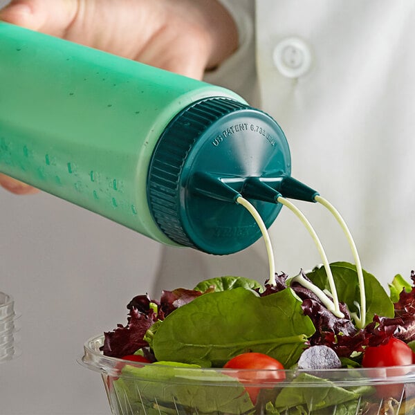 A hand using a Vollrath green Tri Tip squeeze bottle to pour dressing over a salad.