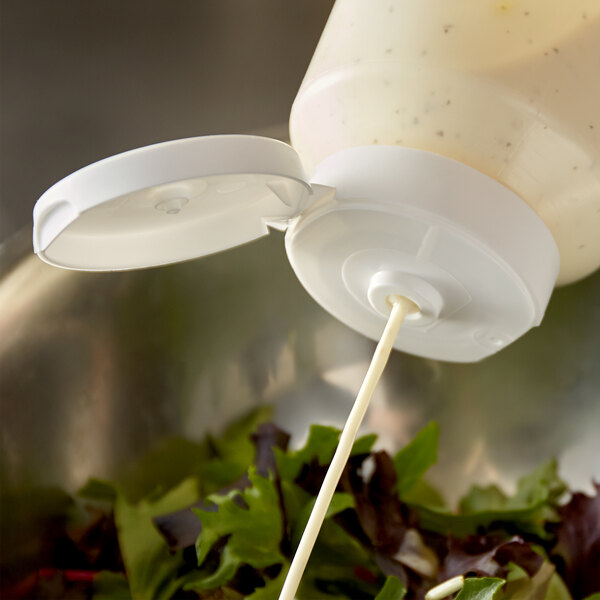 A salad being poured from a Vollrath Flowcut bottle with a white lid.