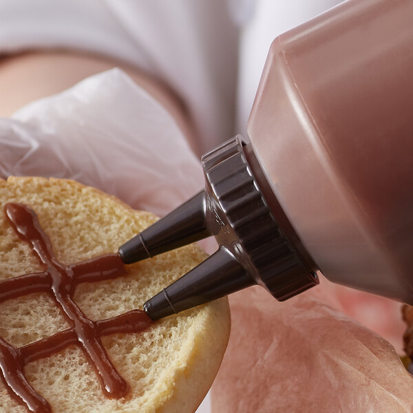 A person putting chocolate sauce on a pastry using a Vollrath Twin Tip bottle cap.