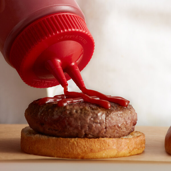 A close-up of a burger with ketchup being poured on it using a Vollrath Traex Twin Tip Wide Mouth Bottle Cap.