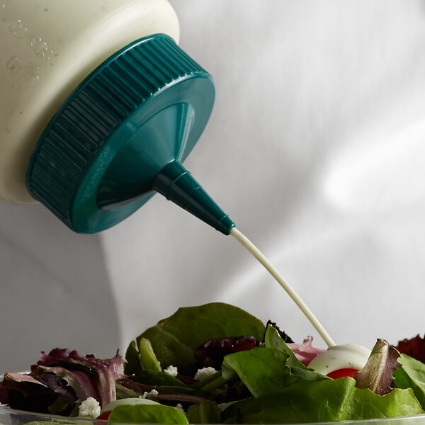 A person pouring dressing from a Vollrath Traex green wide mouth bottle cap onto a salad.