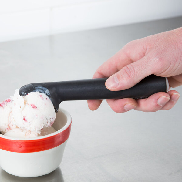 A hand using a Zeroll Zerolon ice cream scoop to serve a scoop of ice cream into a bowl.
