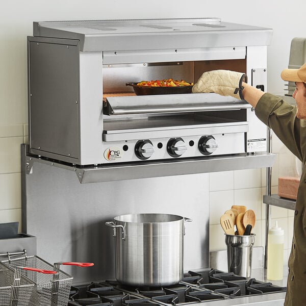 A man using a Cooking Performance Group natural gas salamander broiler in a professional kitchen.