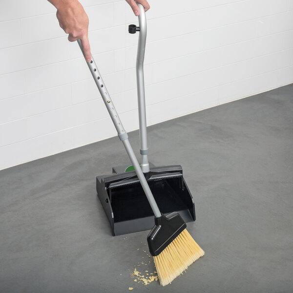 A person using an Unger Ergo angled broom to sweep the floor.