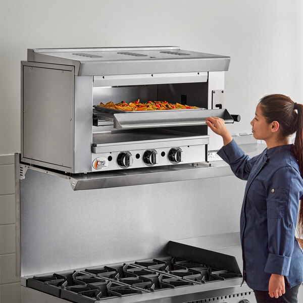 A woman using a Cooking Performance Group natural gas salamander broiler to cook a pizza.