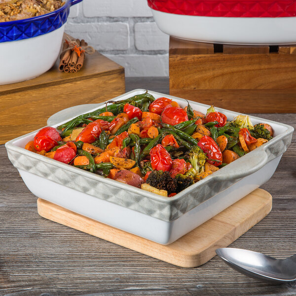 A white Tuxton square casserole dish filled with vegetables on a table.