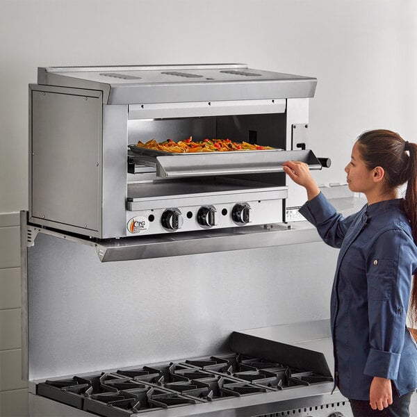 A woman using a Cooking Performance Group infrared salamander broiler in a professional kitchen.