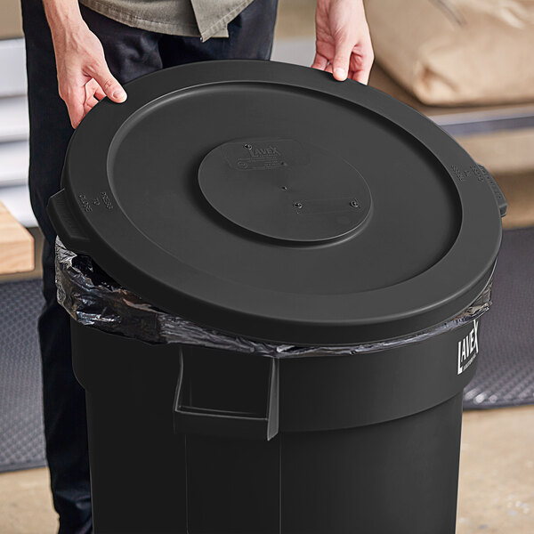 A person holding a Lavex black round commercial trash can lid.