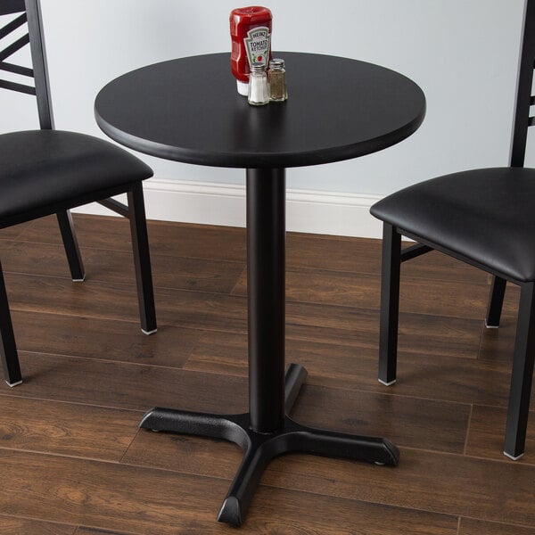 A black Lancaster Table & Seating table with a reversible cherry/black top on a wood floor with two chairs.