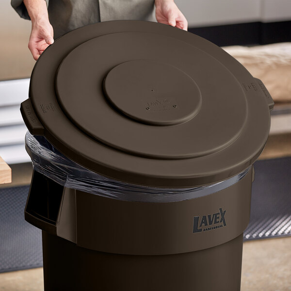A person putting a brown Lavex commercial trash can lid on a brown trash can.