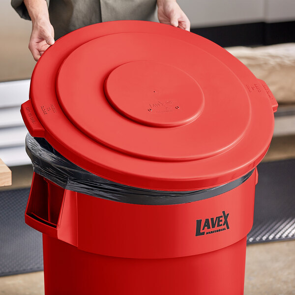 A person holding a Lavex red round commercial trash can lid.