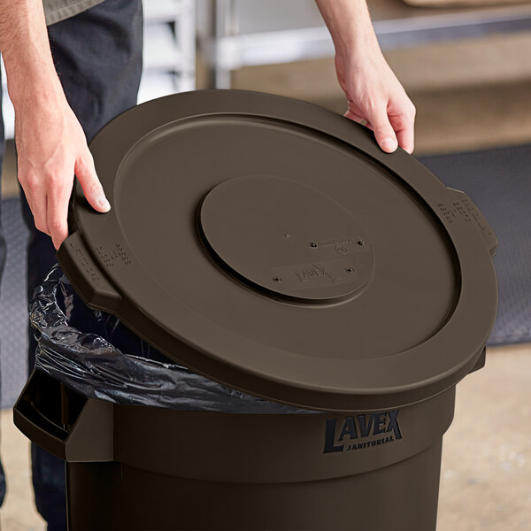 A person opening a Lavex brown round commercial trash can lid.