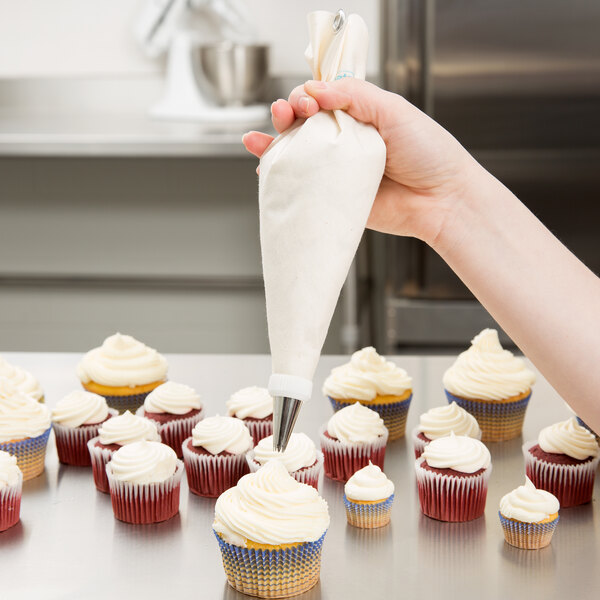 A person using an Ateco plastic coated canvas pastry bag to frost a cupcake.